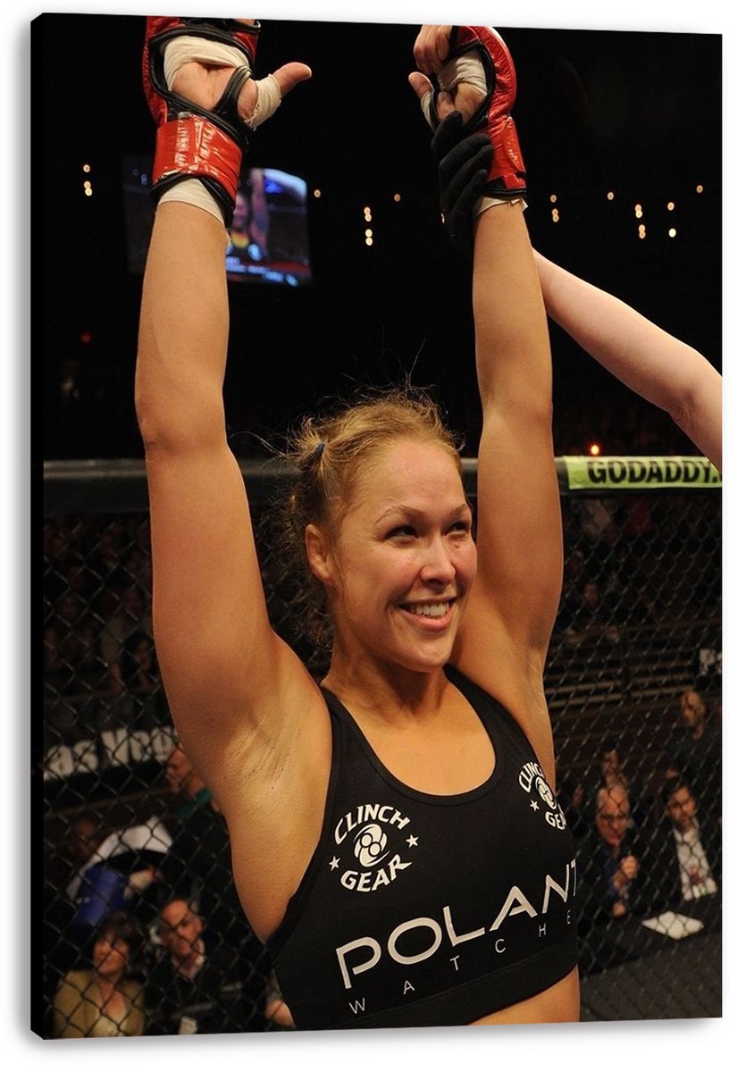 Ronda Rousey canvas wall art print displays the victorious fighter with arms raised, red gloves, cage fencing, and spectators.