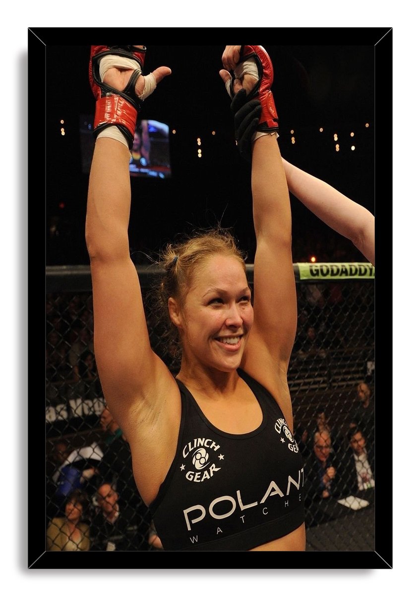 Ronda Rousey framed wall art print features the smiling fighter celebrating with raised red-gloved hands against a dark arena.