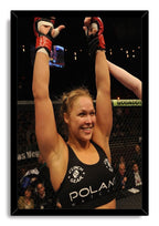 Ronda Rousey framed wall art print features the smiling fighter celebrating with raised red-gloved hands against a dark arena.
