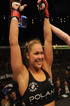Ronda Rousey poster captures the smiling MMA fighter raising taped hands in red gloves inside a dimly lit cage.