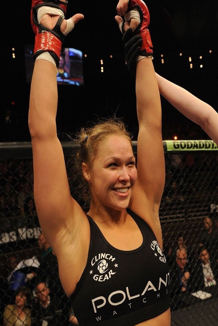 Ronda Rousey poster captures the smiling MMA fighter raising taped hands in red gloves inside a dimly lit cage.