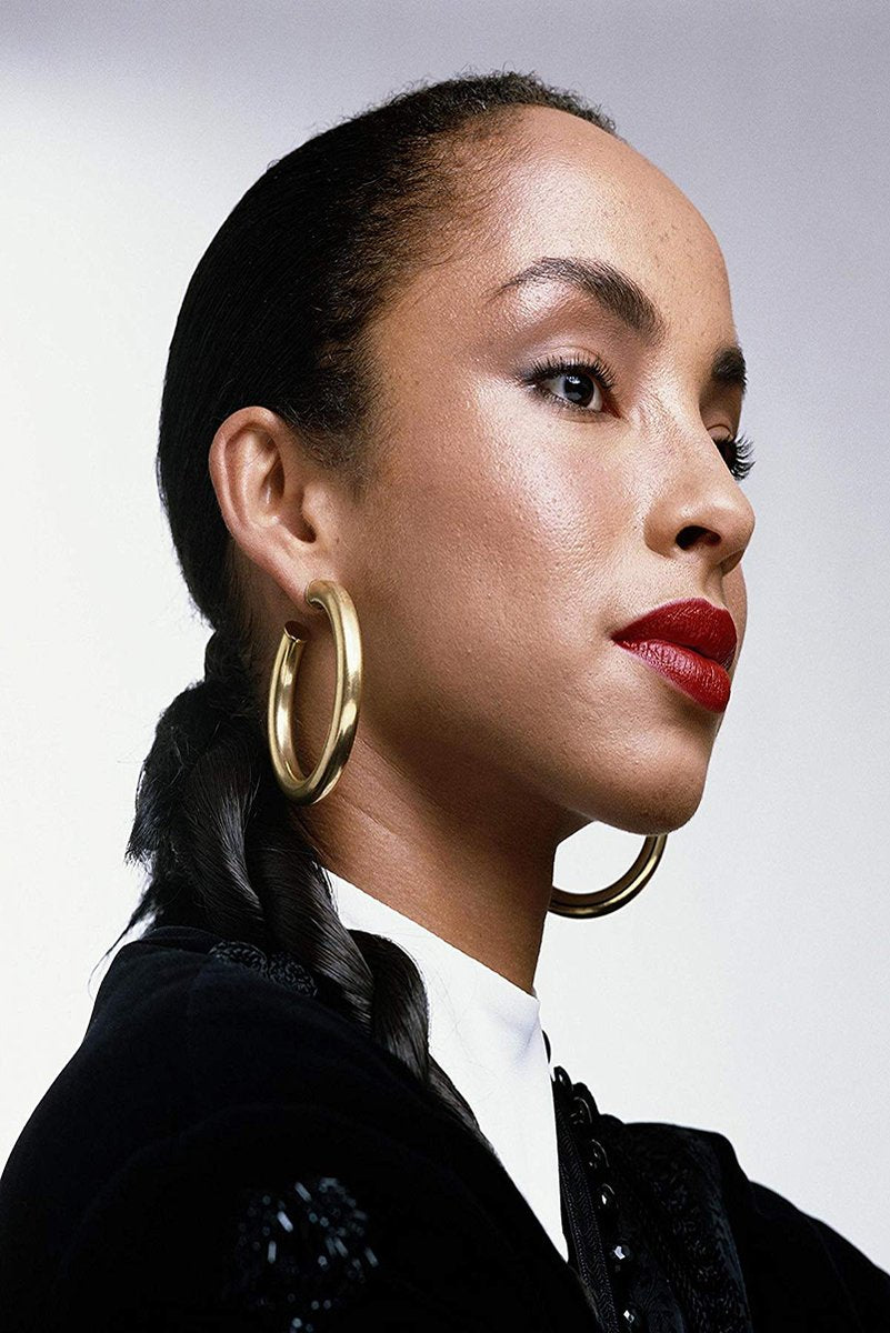 Sade Adu poster portrait in profile, wearing gold hoop earrings, red lipstick, and a black outfit against pale gray.