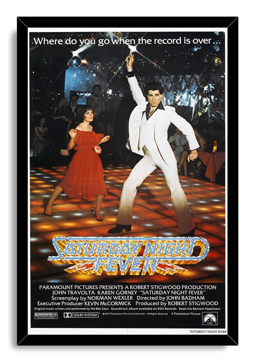 Saturday Night Fever framed wall art print depicts John Travolta striking a dance pose on an amber-lit disco floor beside a woman in red.