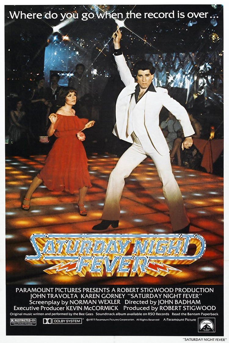 Saturday Night Fever poster features John Travolta in a white suit dancing beside a woman in red on a glowing disco floor.