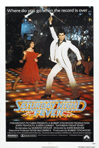 Saturday Night Fever movie poster wall art print featuring John Travolta in a white suit dancing beside a woman in red on a glowing disco floor.