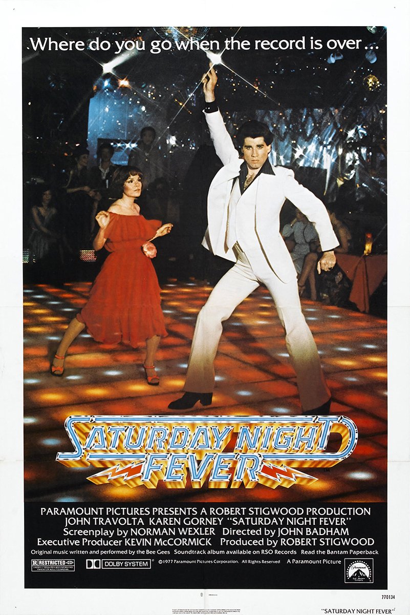 Saturday Night Fever movie poster wall art print featuring John Travolta in a white suit dancing beside a woman in red on a glowing disco floor.