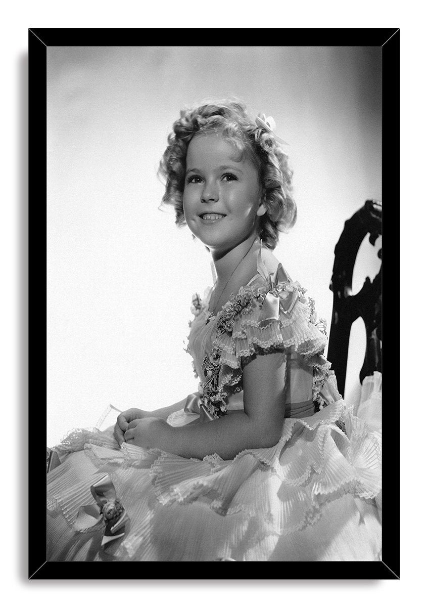 Shirley Temple framed wall art print presents a black-and-white portrait of the smiling child star in a layered dress.