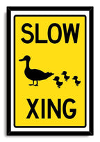 Slow Duck Crossing framed wall art print with a black frame, yellow sign design, and mother duck leading three ducklings.