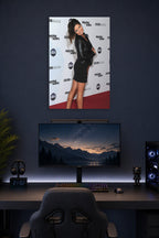 Smiling Maria Menounos in a gaming desk setup above a monitor.