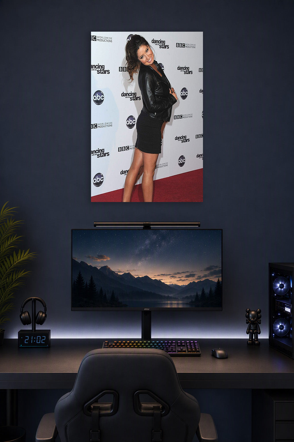 Smiling Maria Menounos in a gaming desk setup above a monitor.
