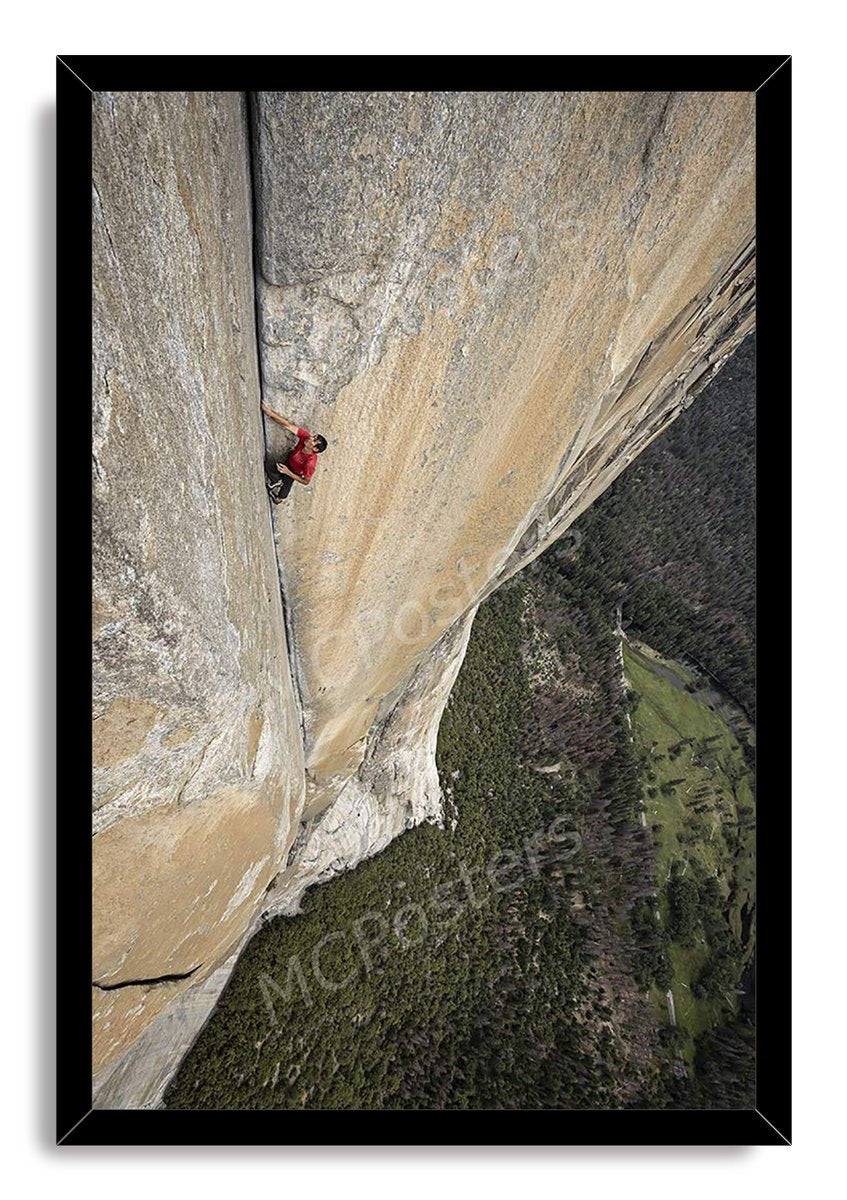 Rock climber framed wall art print presents a lone red-shirted climber scaling a vertical cliff above a forested valley.