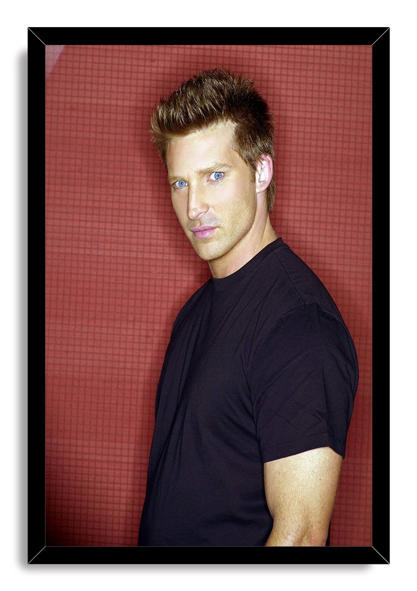 Steve Burton framed wall art print presents a blue-eyed man in a black T-shirt before a red grid backdrop in a black frame.