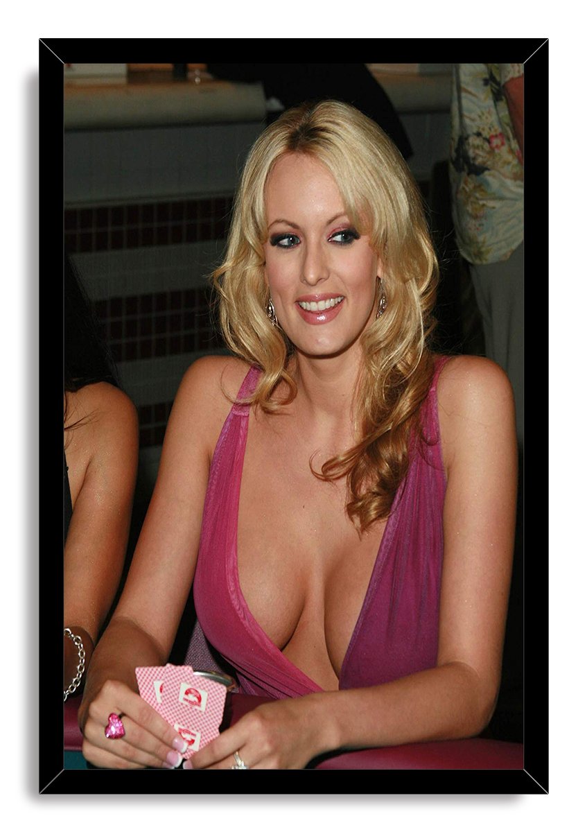 Stormy Daniels framed wall art print portrays her smiling while holding cards at a poker table, set in a black frame.