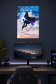 Supergirl in a gaming desk setup above a monitor.