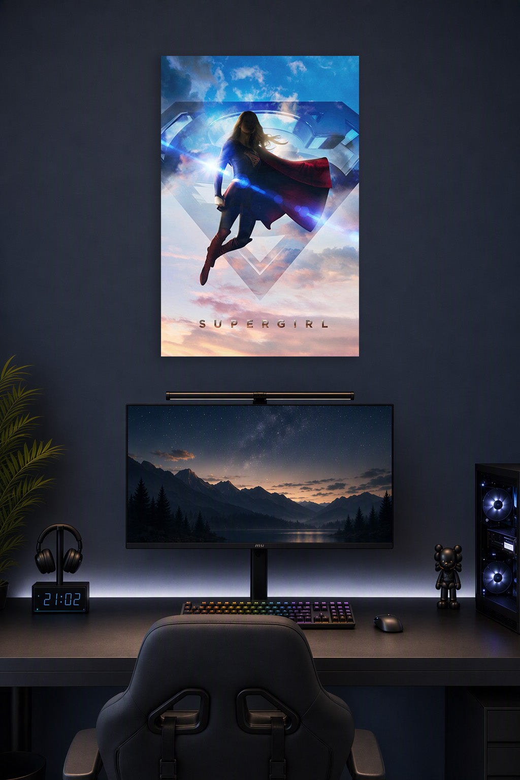 Supergirl in a gaming desk setup above a monitor.