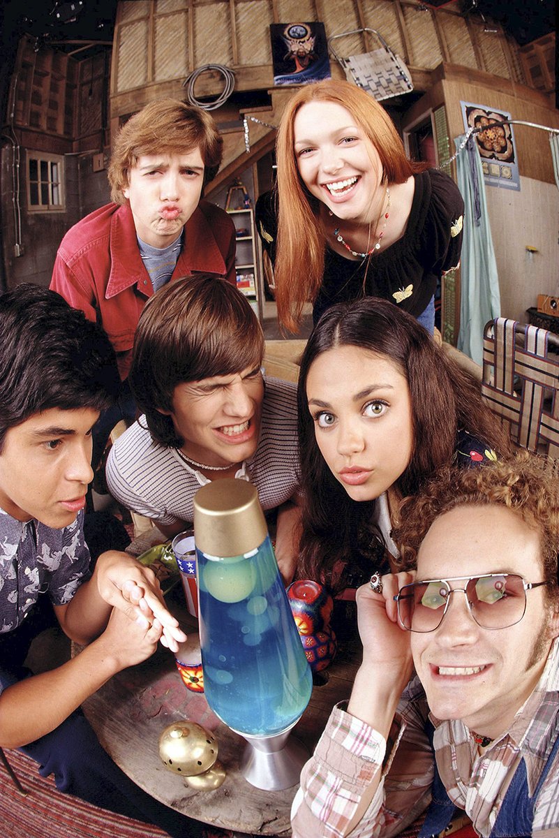 That '70s Show cast poster features six friends crowding around a blue lava lamp in a wood-paneled basement.