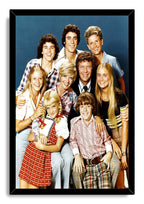 The Brady Bunch cast framed wall art print displays nine smiling actors in colorful retro outfits within a black mitered frame.