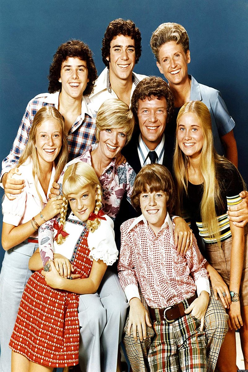 The Brady Bunch cast poster features nine smiling actors in colorful 1970s clothes posed closely against a deep blue backdrop.
