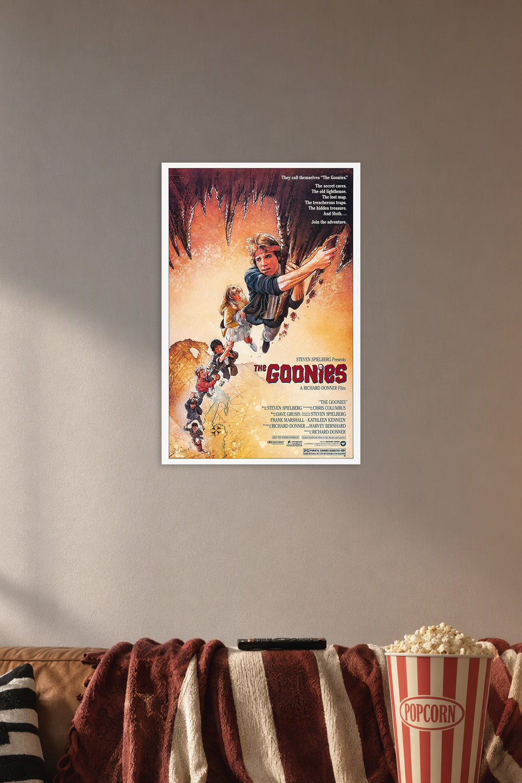 The Goonies Movie Poster in a cozy movie room above a brown sofa with popcorn.