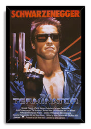 The Terminator framed wall art print features Arnold Schwarzenegger in a leather jacket holding a shotgun beneath red text.