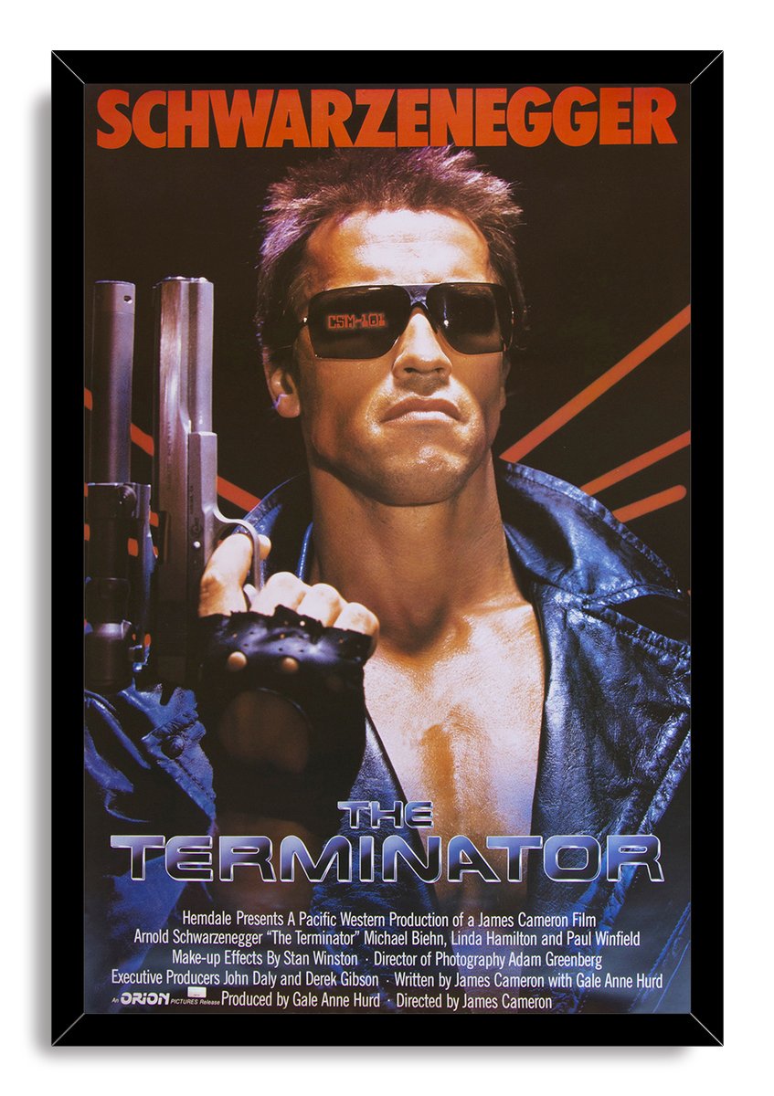 The Terminator framed wall art print features Arnold Schwarzenegger in a leather jacket holding a shotgun beneath red text.