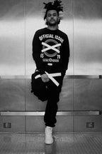 The Weeknd poster in black and white, standing in a metal elevator wearing a graphic sweatshirt and white sneakers.
