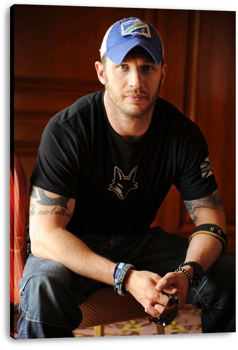 Tom Hardy canvas wall art print featuring the actor seated in a blue cap, black graphic T-shirt, bracelets, and jeans.