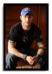 Tom Hardy framed wall art print portraying the actor in a blue cap and black shirt, seated with sunglasses in hand.