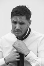 Tom Hardy wall art print in black and white, a close portrait of him adjusting a dark tie over a white shirt.