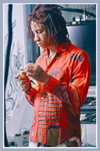 Trippie Redd wall art print portraying the rapper with dreadlocks and face tattoos in a vivid red graphic shirt, looking down while holding a small object.