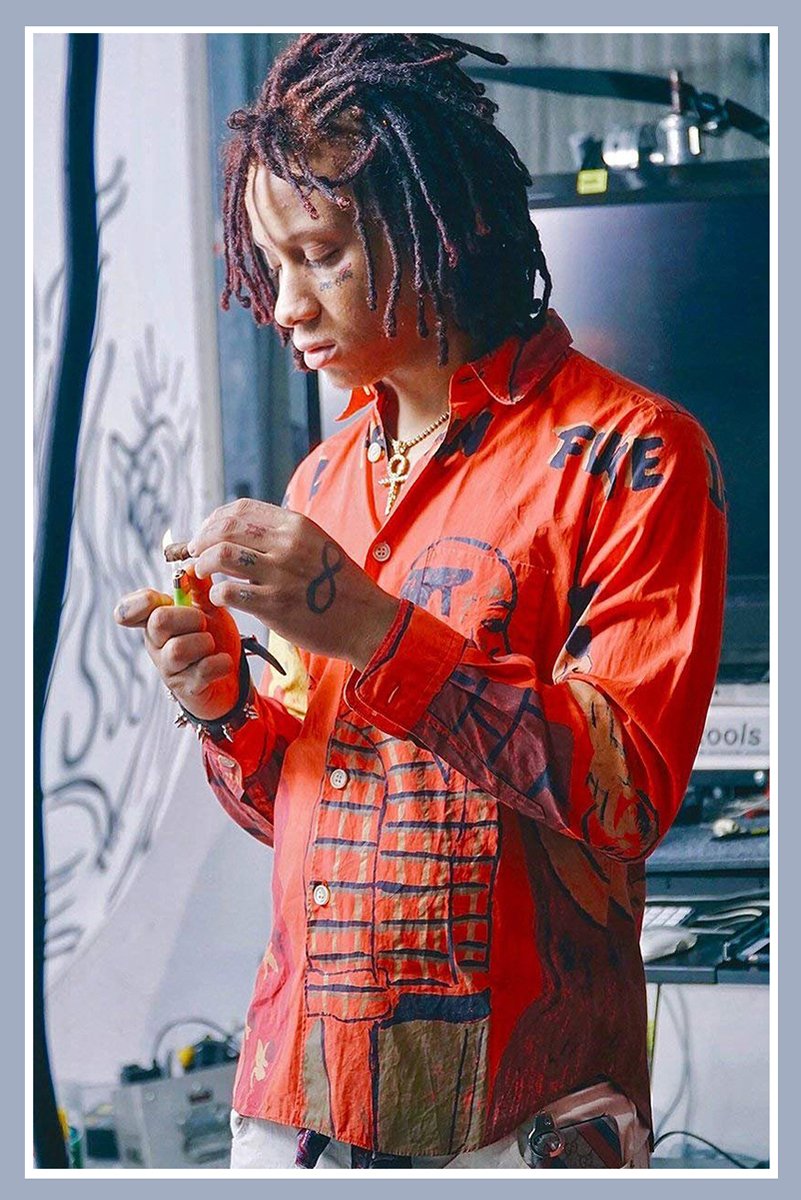 Trippie Redd wall art print portraying the rapper with dreadlocks and face tattoos in a vivid red graphic shirt, looking down while holding a small object.