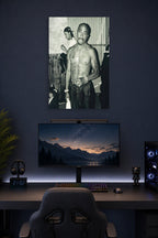 Tupac Shakur in a gaming desk setup above a monitor.