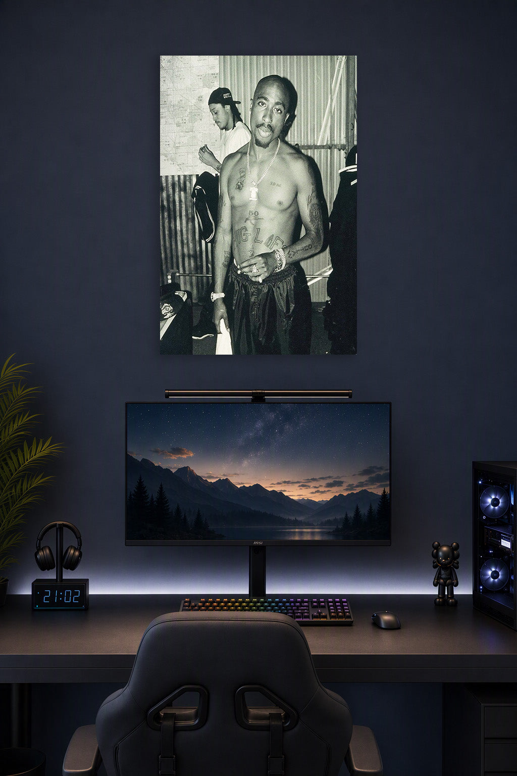 Tupac Shakur in a gaming desk setup above a monitor.