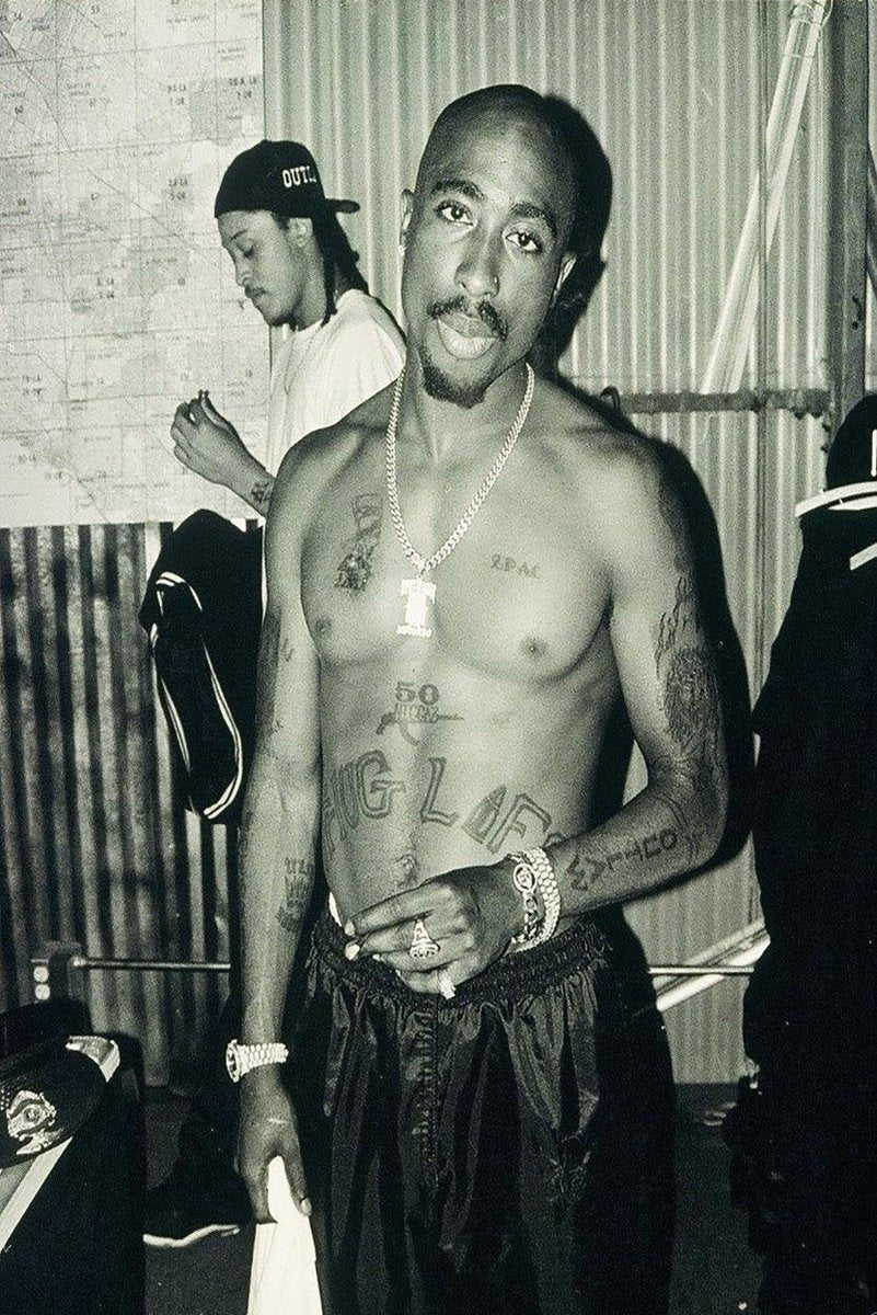 Tupac Shakur poster features a black-and-white full-length portrait of the shirtless rapper wearing chains and watches.