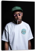 Tyler, The Creator canvas wall art print displays a dark portrait with pink sunglasses, green cap, white T-shirt, and cigarette.