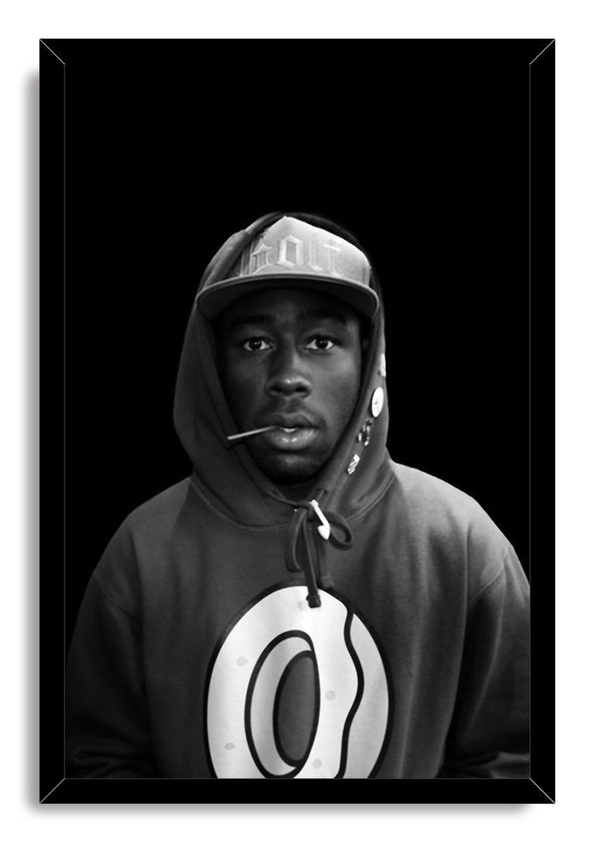 Tyler, The Creator framed wall art print presents a black-and-white portrait of him wearing a cap and logo hoodie.