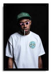 Tyler, The Creator framed wall art print presents a portrait in pink sunglasses and green cap against a deep black background.