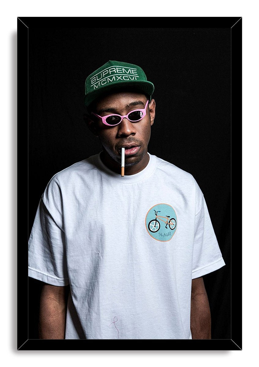 Tyler, The Creator framed wall art print presents a portrait in pink sunglasses and green cap against a deep black background.