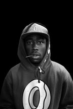 Tyler, The Creator poster features a black-and-white close portrait of him in a cap and logo hoodie against black.