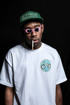 Tyler, The Creator wall art print features a portrait in pink sunglasses, a green cap, and white T-shirt against black.