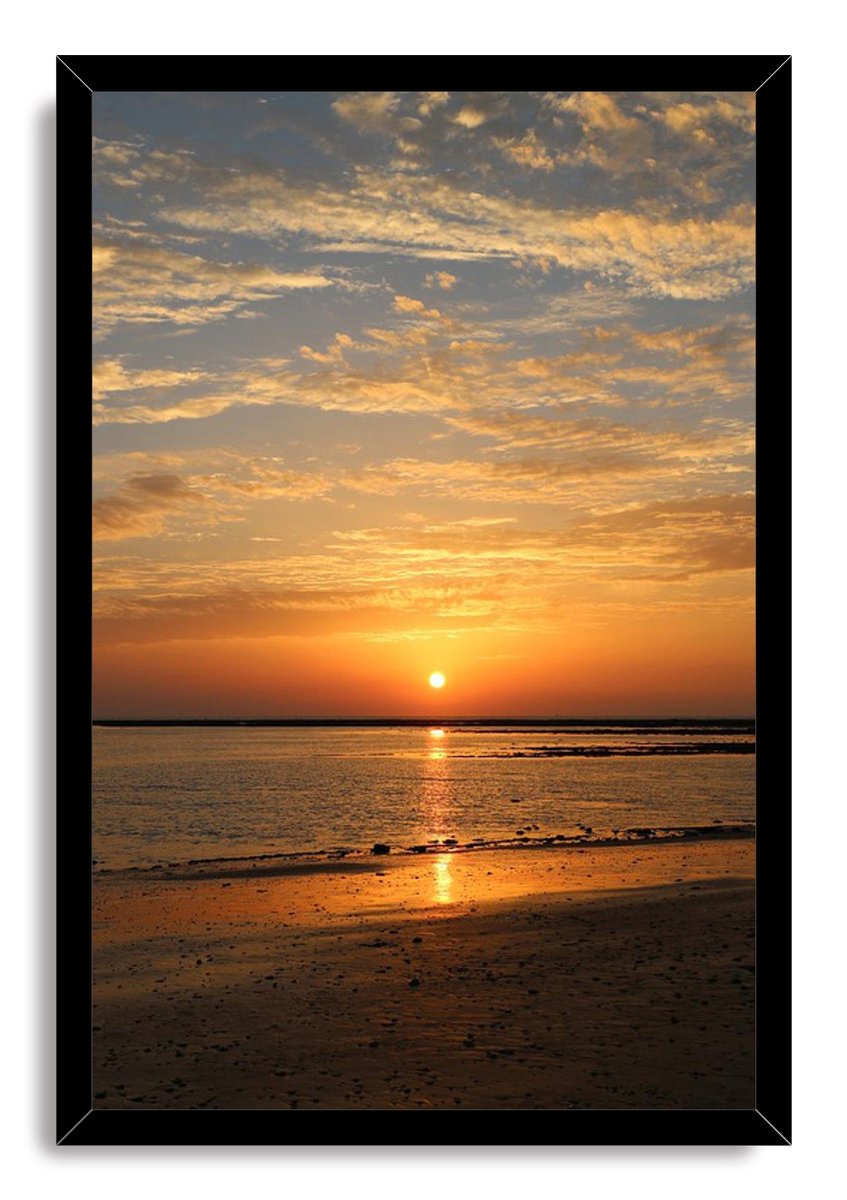 Framed sunset beach wall art print with a black border, golden sunlit water, textured sand, and layered evening clouds.