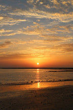 Sunset beach wall art print with a glowing orange sun, gold reflections on shallow water, and cloud-filled sky.