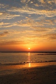 Sunset beach wall art print with a glowing orange sun, gold reflections on shallow water, and cloud-filled sky.