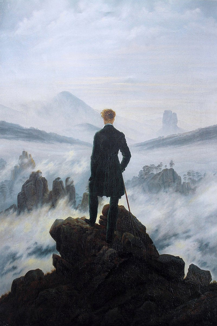 Wanderer Over Foggy Mountains wall art print depicts a man in a dark coat on rocks above misty blue-gray peaks.