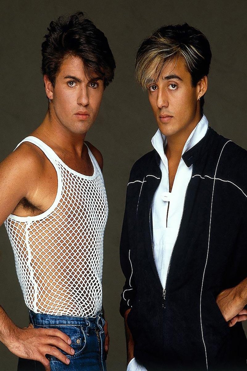 Wham! poster features George Michael and Andrew Ridgeley posing against a dark gray backdrop in distinctive 1980s outfits.