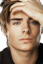 Zac Efron poster close-up portrait with tousled brown hair, gray eyes, and one hand resting across his forehead.